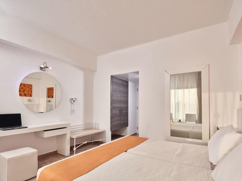 Hell eingerichtetes Schlafzimmer mit weißem Mobiliar, großem Spiegel und orangem Bettüberwurf.