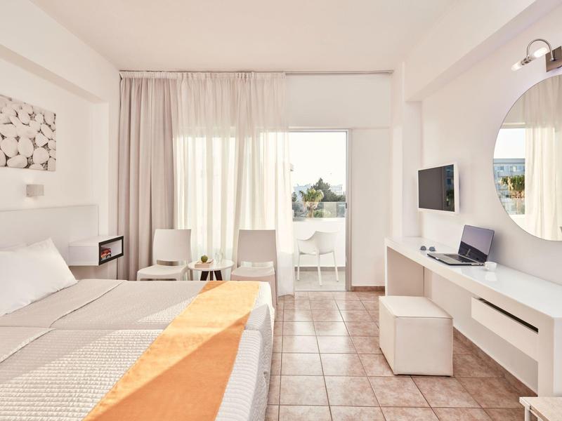 Helles Schlafzimmer mit Doppelbett, Balkon, Fliesenboden, weißer Wand und modernem Mobiliar.