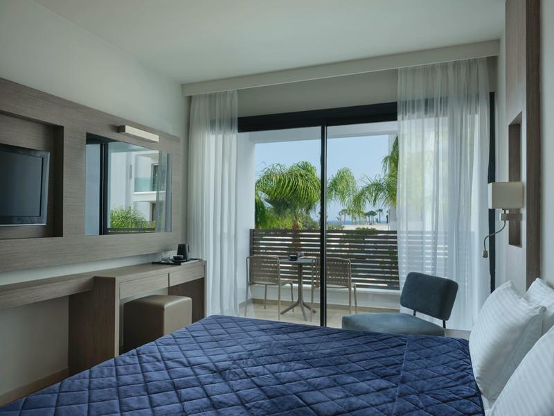 Modernes Schlafzimmer mit blauem Bett, Schreibtisch, Stuhl und Balkon mit Palmenblick.