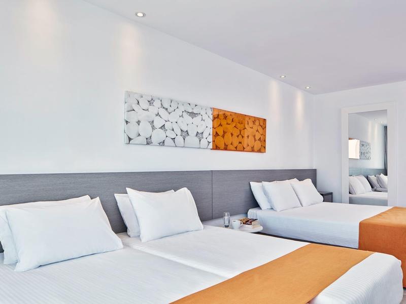 Hell eingerichtetes Schlafzimmer mit zwei Doppelbetten, weißen Wänden und orangen Bettläufern.