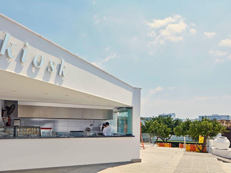 Modernes, weißes Gebäude mit großer Glasfront, klarer Himmel und Blick auf eine Stadt im Hintergrund.