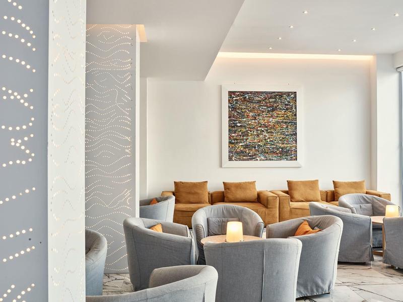Heller Hotel-Lounge mit grauen Sesseln, braunen Kissen und moderner Wandkunst.