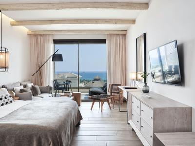 Chambre d'hôtel lumineuse avec lit double, TV, fauteuils et balcon avec vue sur la mer.