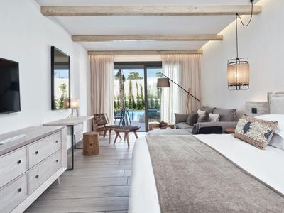 Helles Schlafzimmer mit Doppelbett, weißem Sideboard, grauer Couch und Blick auf Terrasse und Garten.