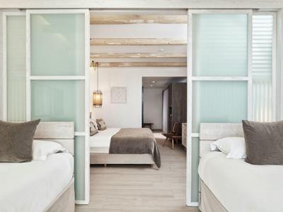 Helles Schlafzimmer mit weißen Wänden, zwei Einzelbetten und breitem Doppelbett durch offene Schiebetüren.