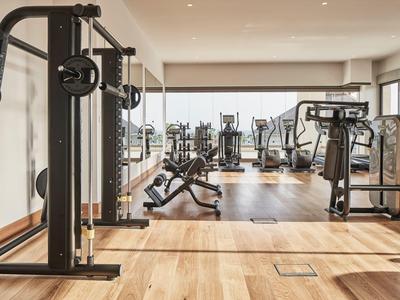 Salle de sport lumineuse avec équipements modernes et sol en bois dans un hôtel.