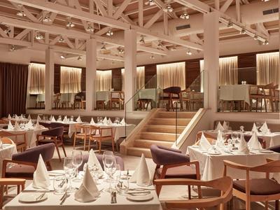 Großer, eleganter Speisesaal mit weißen Tischtüchern, Holzmöbeln und warmem Deckenlicht.