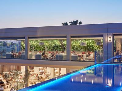 Modernes Gebäude mit großen Fenstern, Blick auf Innenbereich und blauen LED-Lichtern außen bei Dämmerung.