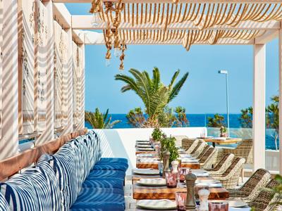 Restaurant en bord de mer avec coussins rayés bleu et blanc, pergola et vue sur la mer en arrière-plan.