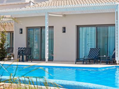 Moderner Bungalow mit Terrasse und Pool, blau-weiße Stühle und große Glas-Schiebetüren.