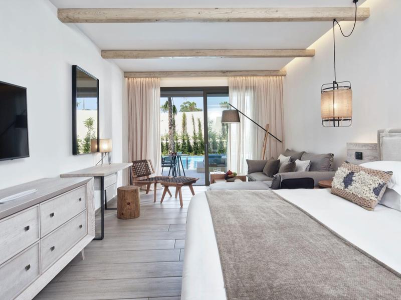 Helles Schlafzimmer mit Doppelbett, weißem Sideboard, grauer Couch und Blick auf Terrasse und Garten.