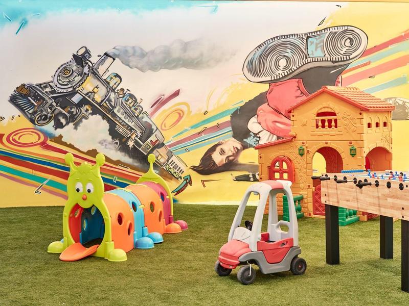 Bunter Spielraum mit Roboter-Wandkunst, Kletterraupe, Spielzeugauto und Tischfußballspiel.