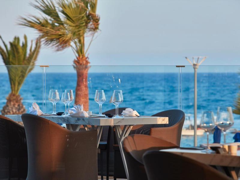 Moderner Außenbereich mit dunklen Stühlen, Glastisch und Blick auf das blaue Meer und Palmen.