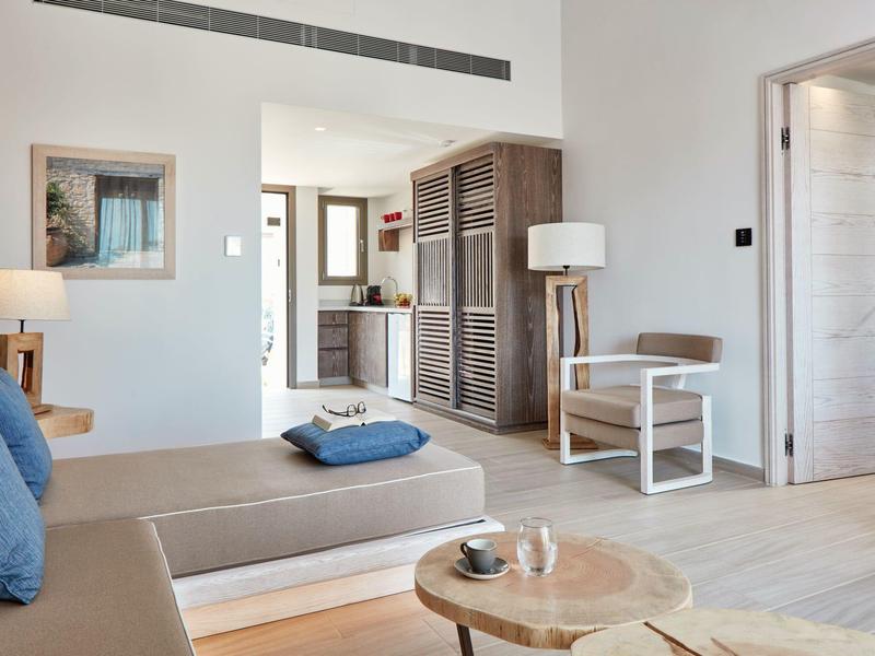 Helles Wohnzimmer mit Holzmöbeln, beigem Sofa und blauen Kissen, offen zum angrenzenden Raum.