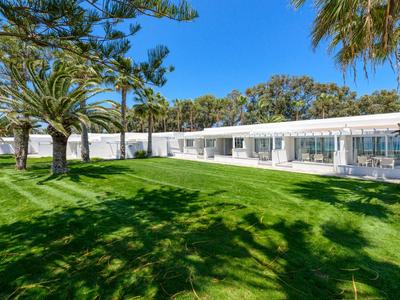 Grand bâtiment d'hôtel blanc à côté d'une pelouse bien entretenue et de palmiers sous un ciel bleu