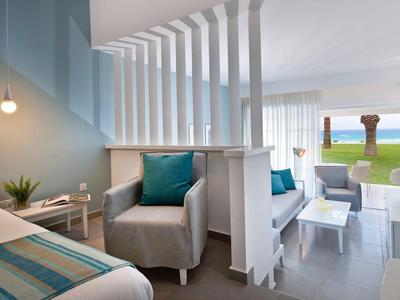 Chambre d'hôtel moderne avec coin salon et vue sur la mer à travers de grandes fenêtres.