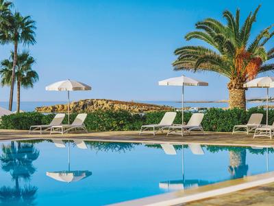 Un espace piscine tranquille avec des transats, parasols et palmiers sous un ciel dégagé.