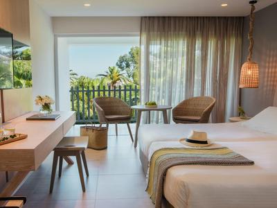 Modernes Hotelzimmer mit zwei Einzelbetten, Holzmöbeln und Balkon mit grünem Ausblick.