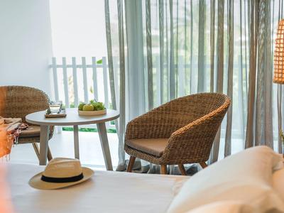 Gemütliche Ecke mit Rattanstühlen, Holzlampe und Tisch vor hellen, transparenten Gardinen.