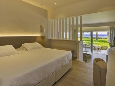 Hell eingerichtetes Schlafzimmer mit zwei Betten, großem Fenster und Blick auf Terrasse und Garten.