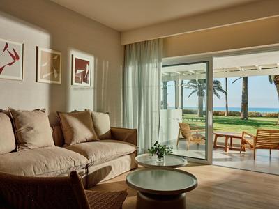 Helles Wohnzimmer mit gemütlichem Sofa, Holzstuhl, rundem Couchtisch und Blick auf Terrasse mit Meer.