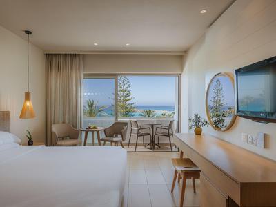 Modernes Hotelzimmer mit Meerblick, Doppelbett, Schreibtisch und Balkon mit Sitzbereich.