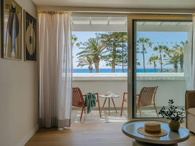 Moderner Hotelbalkon mit Tisch, zwei Stühlen und Blick auf Meer und Palmen.