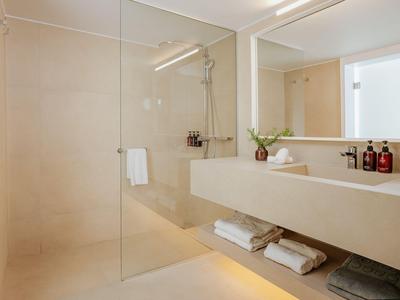 Helle moderne Badezimmerecke mit Glasdusche, großem Spiegel und minimalistischem Waschbecken.