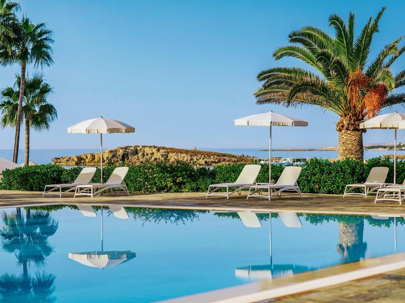 Ruhepool mit Liegestühlen, weißen Sonnenschirmen, Palmen und klarem blauem Himmel.