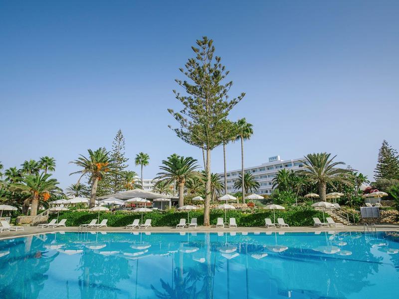 Großer blauer Pool mit weißen Liegestühlen, tropischen Palmen und klar blauem Himmel im Hintergrund.