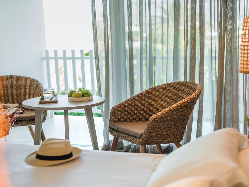 Gemütliche Ecke mit Rattanstühlen, Holzlampe und Tisch vor hellen, transparenten Gardinen.