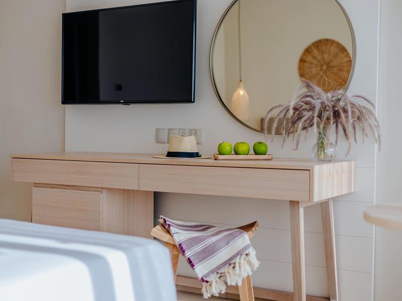 Moderner Tisch mit hellem Holz, Spiegel, TV und einem Stuhl mit Decke in einem hellen Raum.