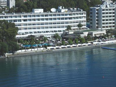 Großes Hotel am Wasser mit mehreren Pools und Liegestühlen, umgeben von grünen Bäumen.
