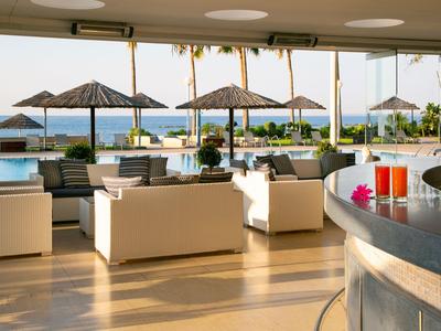 Area lounge moderna dell'hotel con posti a sedere e vista su piscina e mare con ombrelloni.