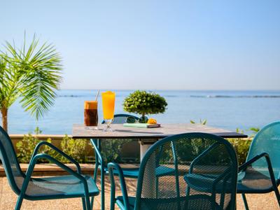 Terrazza con tavolo e sedie vicino all'acqua, bevande e palma visibili.