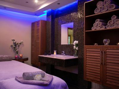 Ein ruhiger Spa-Raum mit Massageliege, Handtüchern, Holzregalen und sanfter blauer Beleuchtung.