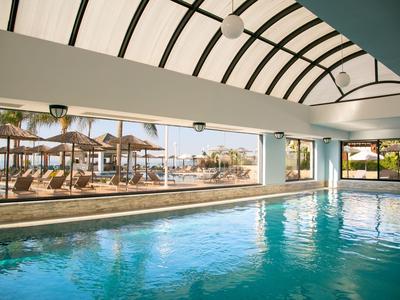 Piscina interna con tetto in vetro e vista su lettini sulla spiaggia.