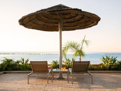 Zwei Liegestühle unter einem großen Strohmantelschirm mit Blick auf das Meer bei Sonnenuntergang.