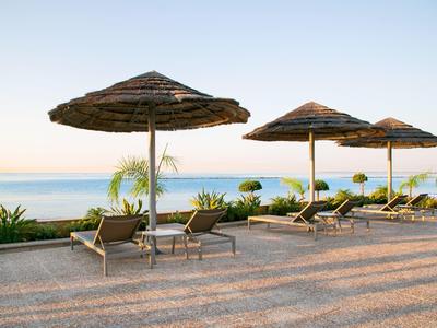 Strandliegen mit Strohschirmen neben ruhigem Meer und klar blauem Himmel bei Sonnenaufgang.