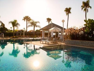 Tramonto presso una piscina con palme e un gazebo in una struttura alberghiera.