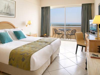 Hell eingerichtetes Schlafzimmer mit Doppelbett, Balkon und Meerblick, cremefarbene Fliesen und Holz.