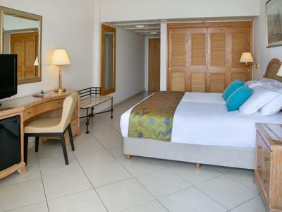 Helles Hotelzimmer mit großem Bett, Schreibtisch, Stuhl, TV und Holzschrank.