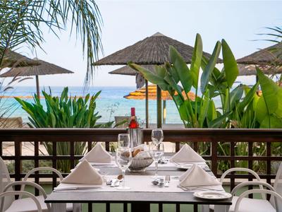 Area pranzo all'aperto con tavolo apparecchiato, vista su ombrelloni da spiaggia e mare sullo sfondo