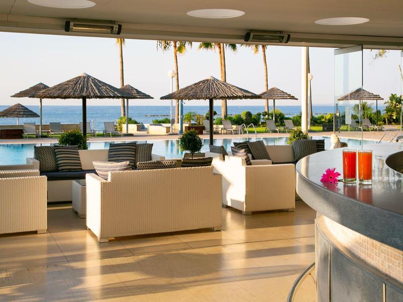 Moderner Außenbereich mit weißen Sitzmöbeln, Sonnenschirmen und Blick aufs Meer bei sonnigem Wetter.