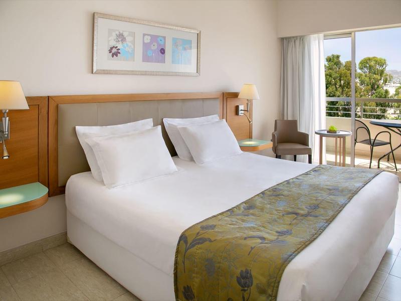 Helles Schlafzimmer mit großem Bett, Holzmöbeln, weißer Bettwäsche und Terrasse mit Gartenblick.