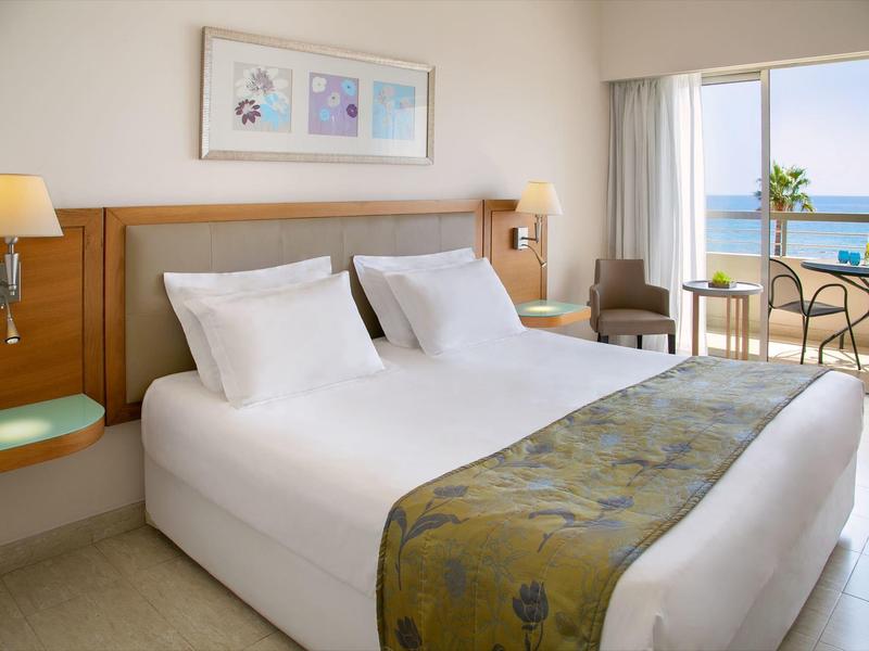 Modernes Hotelzimmer mit großem Bett, weißer Bettwäsche und Balkon mit Meerblick.