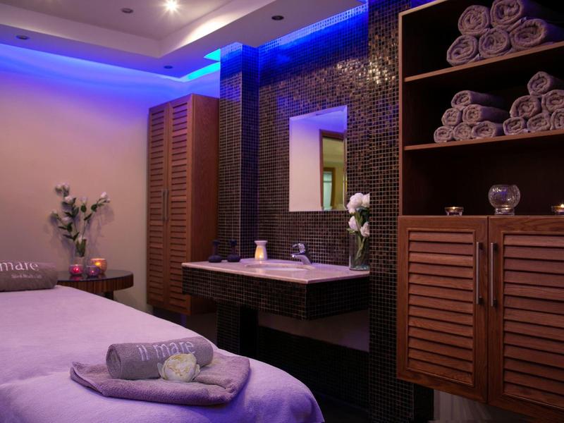 Ein ruhiger Spa-Raum mit Massageliege, Handtüchern, Holzregalen und sanfter blauer Beleuchtung.