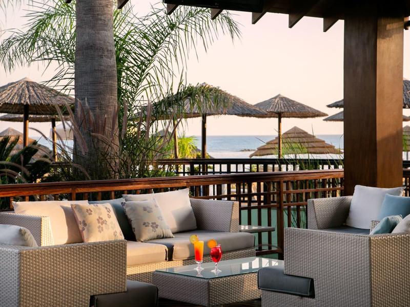 Gemütliche Lounge mit Rattanmöbeln, Kissen und Blick aufs Wasser bei Sonnenuntergang.