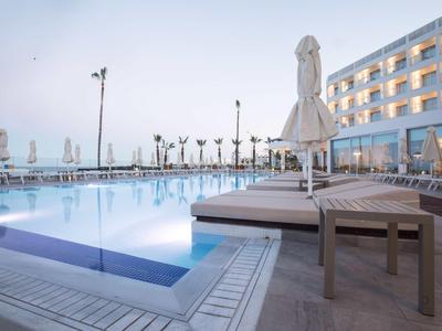 Moderner Hotelpool mit Liegestühlen und Blick auf das Meer bei klarem Himmel.