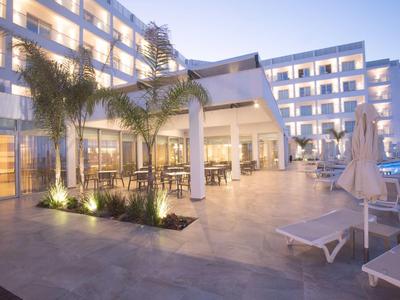 Modernes Hotel mit großem Außenbereich, Poolliegen, Palmen und Glasfassade bei Dämmerung.